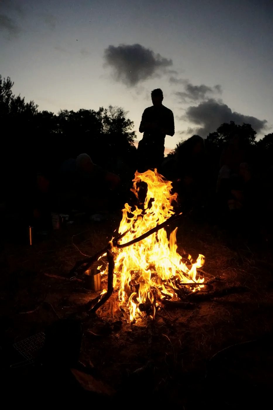A fire after dark, a figure beyond it